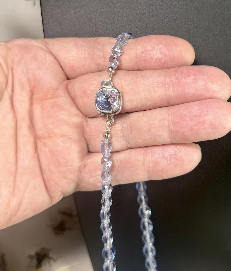 May include: A delicate necklace featuring a light blue, square-cut gemstone pendant set in a silver bezel. The necklace is strung with small, faceted, light blue beads. The design is elegant and suitable for special occasions.