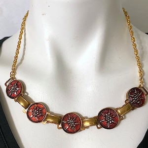 May include: A gold chain necklace with five red and silver enamel pendants featuring a starburst design.