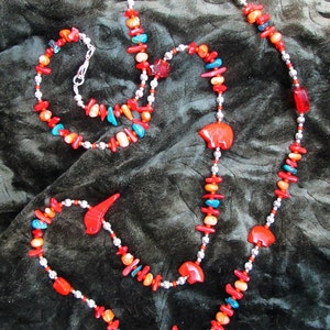 May include: A long silver chain necklace with red, orange, and turquoise beads. The necklace features several carved bear and bird charms.