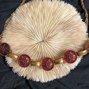 May include: A gold chain necklace with five red and gold star-shaped pendants. The necklace is lying on a white coral-like surface.