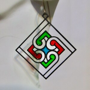 Könnte beinhalten: Ein Paar geometrische Ohrringe mit schwarzem Rand und buntem Emaille. Die Ohrringe sind quadratisch mit einem kleineren Quadrat im Inneren. Das kleinere Quadrat ist mit einem Muster aus vier geschwungenen Linien in Rot, Grün und Blau gefüllt.