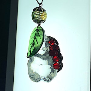 May include: A glass pear ornament with a green leaf and red beads. The pear is clear and the beads are a deep red. The ornament is hanging from a metal loop.