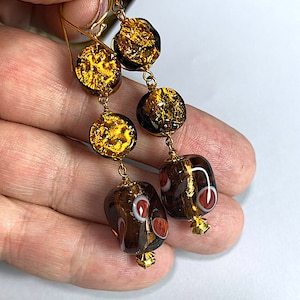 May include: Gold tone dangle earrings with brown and gold glass beads. The beads have a textured, metallic finish and some have white and red accents.