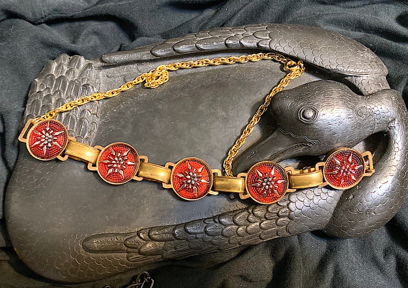 May include: A gold chain necklace with five red and gold round medallions. Each medallion features a stylized starburst design.