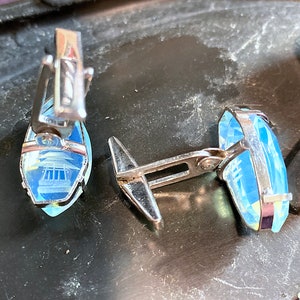 Może przedstawiać: Para srebrnych spinek do mankiet&oacute;w z niebieskimi szklanymi wstawkami. Szklane wstawki mają geometryczny wz&oacute;r.