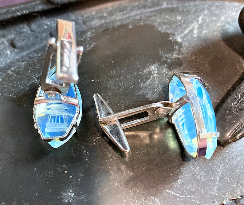 Może przedstawiać: Para srebrnych spinek do mankiet&oacute;w z niebieskimi szklanymi wstawkami. Szklane wstawki mają geometryczny wz&oacute;r.