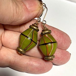 May include: A pair of green glass bead earrings with gold accents. The beads have a striped pattern in white, orange, and black.
