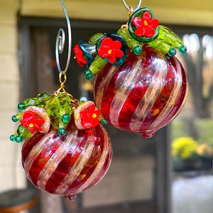 May include: Two red and gold striped glass ornaments with green and red glass beads and flowers. The ornaments are hanging from silver hooks.