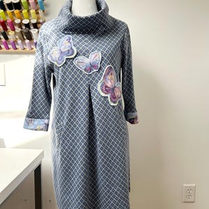 May include: A blue dress with a cowl neck and a geometric pattern. The dress has three butterfly appliques on the front.