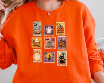 Può includere: Una felpa girocollo arancione brillante con una stampa grafica centrale composta da nove disegni rettangolari a forma di francobollo. Le illustrazioni includono un calderone, un fantasma, una zucca, caramelle, una lapide, una casa stregata, una strega e un gatto nero.