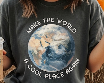 May include: A charcoal gray t-shirt featuring a circular graphic of the Earth in the center. The text "MAKE THE WORLD A COOL PLACE AGAIN" is printed in white capital letters in a circular arc around the planet illustration.