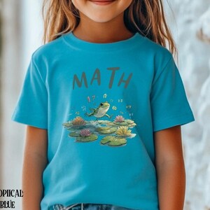 May include: A turquoise t-shirt with the word "MATH" in grey letters. The shirt features a cartoon frog on lily pads with numbers. The words "TROPICAL BLUE" are printed at the bottom of the shirt.