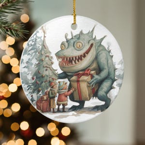 Può includere: Ornamento natalizio rotondo con un'illustrazione fantastica di un mostro amichevole che offre regali ai bambini vicino a un albero di Natale decorato. Il mostro è blu-verde con denti affilati. L'ornamento ha una corda d'oro.