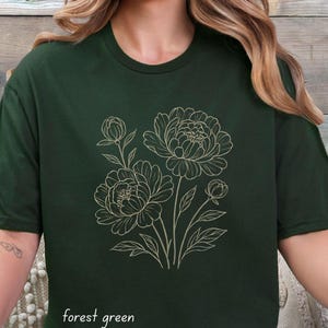 May include: Dark green t-shirt with a gold outline floral design of peonies. The shirt has a round neck and short sleeves. The words "forest green" are printed at the bottom of the shirt.