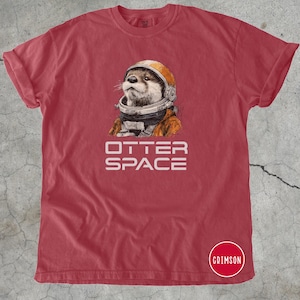 K&ouml;nnte beinhalten: Rotes T-Shirt mit einer Illustration eines Otters, der einen Astronautenhelm und -anzug tr&auml;gt. Der Text "OTTER SPACE" ist darunter gedruckt. Das T-Shirt hat hochgekrempelte &Auml;rmel und einen Rundhalsausschnitt.