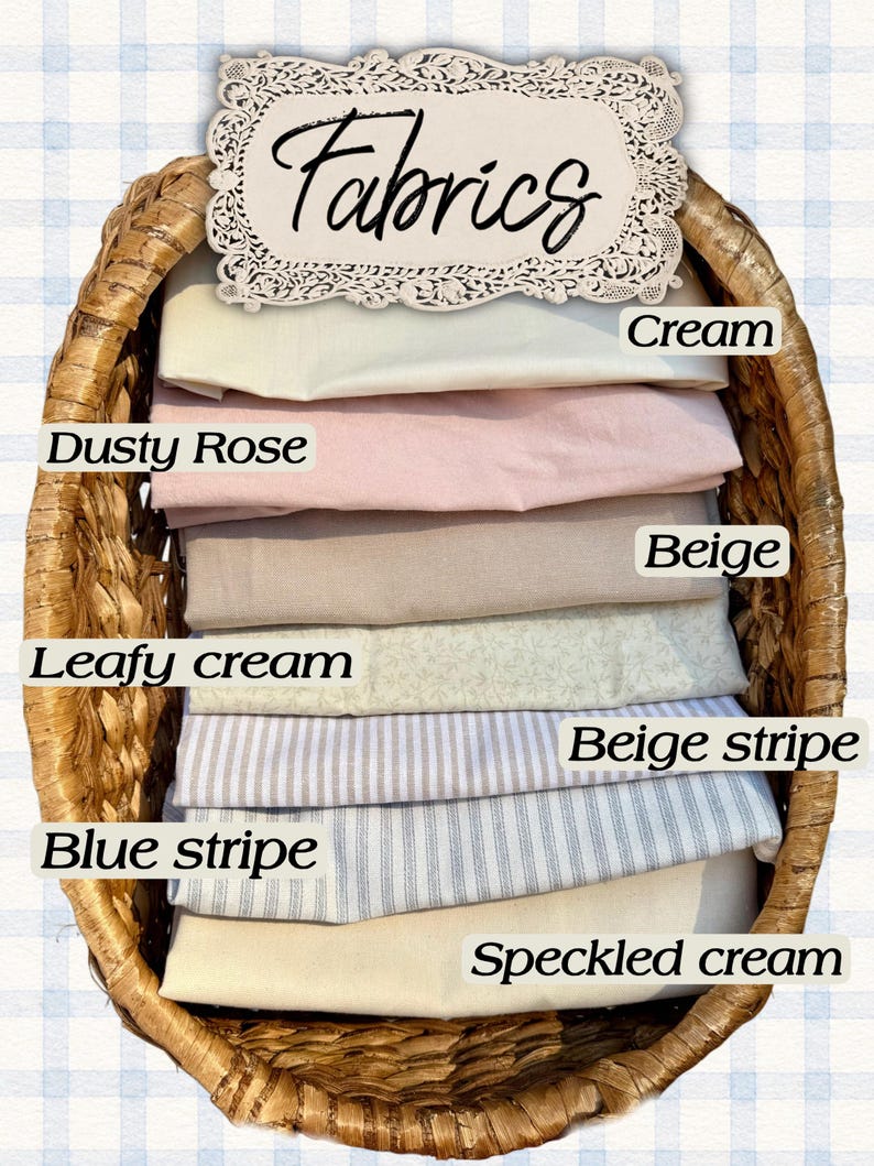 May include: A woven wicker basket containing folded fabric swatches labeled Cream, Dusty Rose, Beige, Leafy cream, Beige stripe, Blue stripe, and Speckled cream. A decorative sign at the top displays the word Fabrics in a script font.