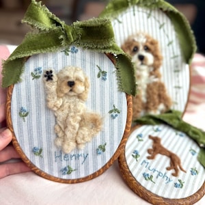 May include: Three oval embroidery hoops featuring needle-felted dog portraits on blue and white striped fabric. Each hoop is topped with a green velvet ribbon and decorated with embroidered blue flowers. The names Henry and Murphy are stitched below.