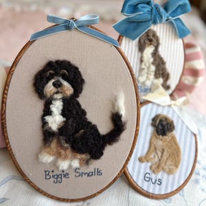 May include: Three oval embroidery hoops featuring needle-felted dog portraits. The largest hoop displays a black, white, and tan dog with the text Biggie Smalls. Two smaller hoops show a brown and white dog and a tan dog named Gus.