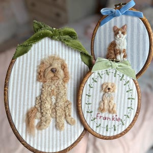 May include: Three oval wooden embroidery hoops featuring needle-felted animal portraits on striped fabric. One hoop displays a golden dog with a green velvet bow, another a ginger cat with a blue ribbon, and the third a small dog named Frankie.
