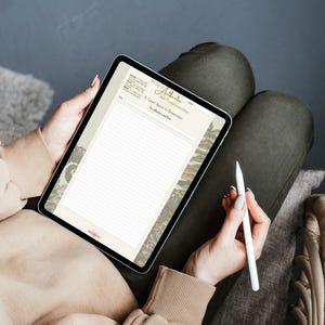 May include: A digital tablet displaying a lined journal page with botanical illustrations and the text "Authentic Self Transformation". The tablet is held by a person wearing a beige sweater, with a white stylus in hand. The background is a muted gray.