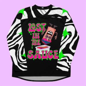 May include: A long-sleeve jersey featuring a black centre panel with the text LOST IN THE SAUCE in pink with green drips. A cartoon character dips into a white container of colourful sauce. The sleeves have a black and white wavy zebra pattern.