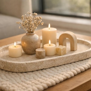 Puede incluir: Una composición decorativa sobre una mesa de madera. Presenta velas encendidas, un pequeño jarrón con flores secas y un arco de madera, todo sobre una bandeja beige. Un camino de mesa texturizado completa la escena.