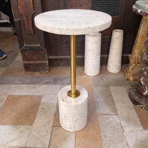 May include: A small, round side table with a white stone top and base, connected by a gold-coloured metal stem. The table is approximately 50 cm tall. The design is simple and elegant, suitable for various interior styles.
