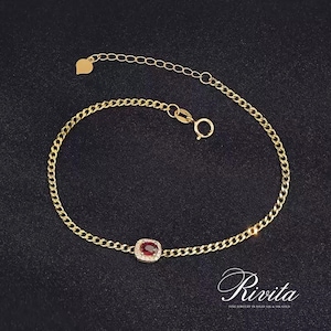 Puede incluir: Pulsera dorada con una gema roja central, rodeada de pequeñas piedras blancas. La pulsera tiene un diseño de cadena delicado y un dije en forma de corazón. La marca "Rivita" se muestra en la esquina inferior derecha.