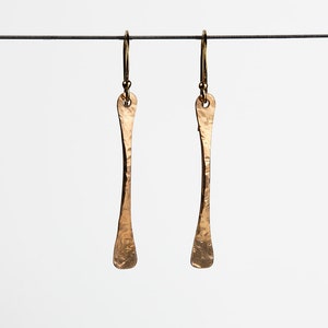 May include: A pair of gold-toned earrings with a hammered texture and a long, thin, slightly curved shape.