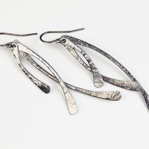 May include: A pair of silver earrings with a hammered texture and a long, thin, curved design.