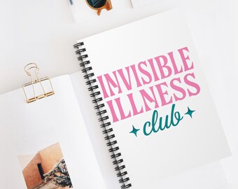 May include: A white spiral-bound notebook with the text "INVISIBLE ILLNESS club+" in pink and teal. The notebook is open, revealing a photo and a gold binder clip. Sunglasses and a pen are also visible.