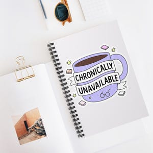 Pode incluir: Um autocolante com uma caneca de café roxa clara com a frase "Chronically Unavailable" numa faixa. A caneca está cheia de líquido castanho e decorada com estrelas, livros e óculos. O autocolante está num caderno espiral branco.