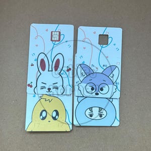May include: Four white rectangular cards with cartoon animal designs. Two cards feature a white bunny and a yellow chick. The other two cards have a purple bunny and a blue character. Each card has a small square and the number "17".