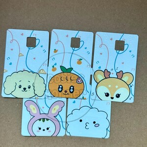 May include: A collection of six rectangular cards with cartoon animal faces. The cards feature a dog, an orange, a deer, a bunny, and a cloud. Each card has a square cutout and is decorated with hearts and the number "17".