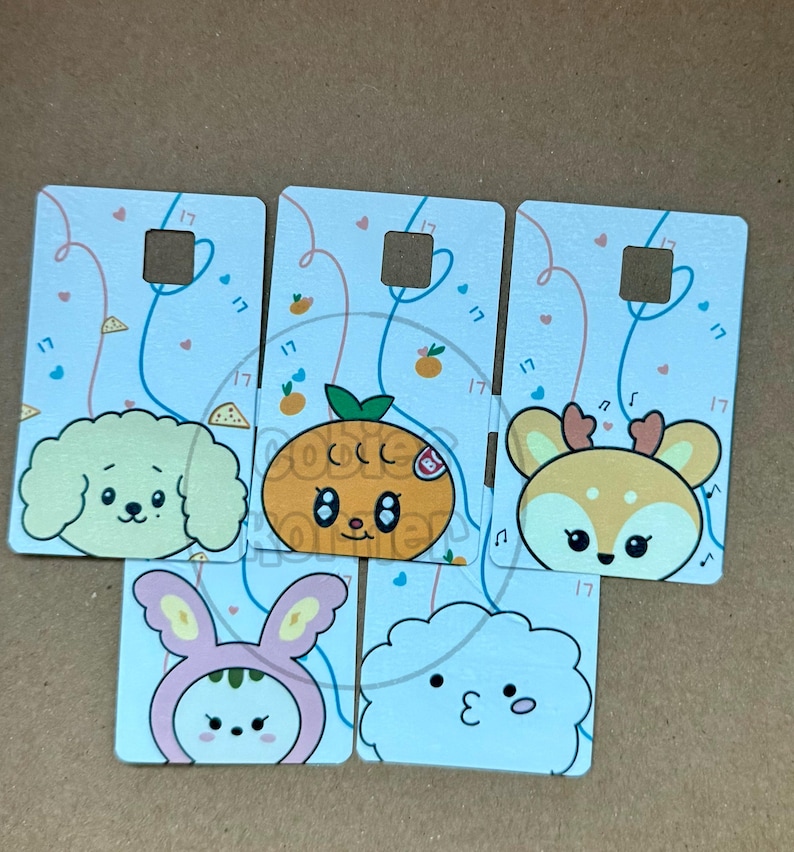 May include: A collection of six rectangular cards with cartoon animal faces. The cards feature a dog, an orange, a deer, a bunny, and a cloud. Each card has a square cutout and is decorated with hearts and the number "17".