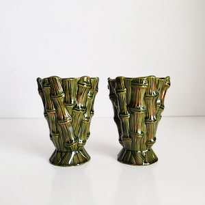 May include: A pair of green ceramic vases with a bamboo design. The vases are tall and slender, with a flared top and a rounded base.