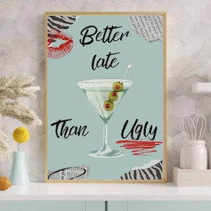 May include: A framed art print with a light blue background features a martini glass with olives and the text "Better late than ugly." The artwork includes lipstick, zebra print, and newspaper clippings.