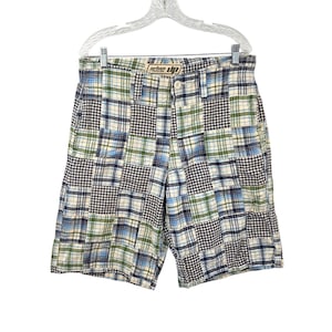 May include: Patchwork plaid shorts in shades of blue, green, and white, hanging on a white hanger. The shorts feature a button closure and the "urban up" logo on the waistband. The shorts are a casual style.