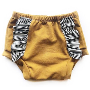 May include: Mustard yellow baby bloomers with black and white striped ruffle trim.