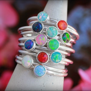 May include: A stack of silver rings with colourful opal gemstones. The rings are arranged in a cone shape, with the largest ring at the bottom and the smallest ring at the top. The opals are in various colours, including blue, green, red, and pink.