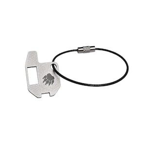 May include: A silver-colored key chain with a paw print design. The key chain has a rectangular opening and a black wire loop with a metal clasp. The paw print is in the center of the key chain.