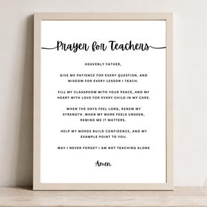 May include: A framed wall art print featuring the black text Prayer for Teachers followed by a prayer in English, ending with the word Amen. The frame is a light wood color, and the background of the print is white. The text is in a mix of serif and script fonts.