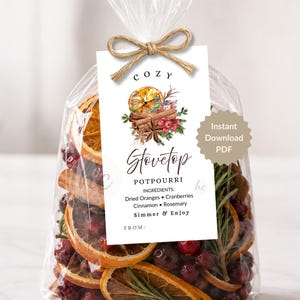 May include: A clear cellophane bag filled with dried oranges, cranberries, and rosemary, tied with twine. A tag reads "COZY Stovetop Potpourri" with ingredients listed. A decorative illustration of oranges, cinnamon, and flowers is on the tag.