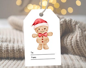May include: A white rectangular gift tag with a hole at the top and a grey string. The tag features a watercolor illustration of a gingerbread person wearing a red Santa hat and a red bow tie. Below the figure are the printed words To: and From:.