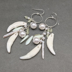 May include: A pair of dangle earrings featuring silver-toned wire hoops with hanging white curved tusk-like charms, lustrous white spherical beads, elongated pale iridescent accents, and small translucent light green faceted beads.