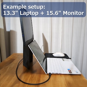 Puede incluir: Un portátil de 13,3" conectado a un monitor de 15,6" en un escritorio de madera. El portátil está abierto e inclinado hacia arriba, con un ratón inalámbrico blanco sobre una alfombrilla de ratón negra.