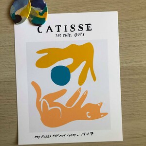 May include: A white print with a yellow, orange, and blue abstract design. The print has the text "CATISSE THE CUTE. OUTS" and "MY PURES ARE NOT CRAZY - 1947".