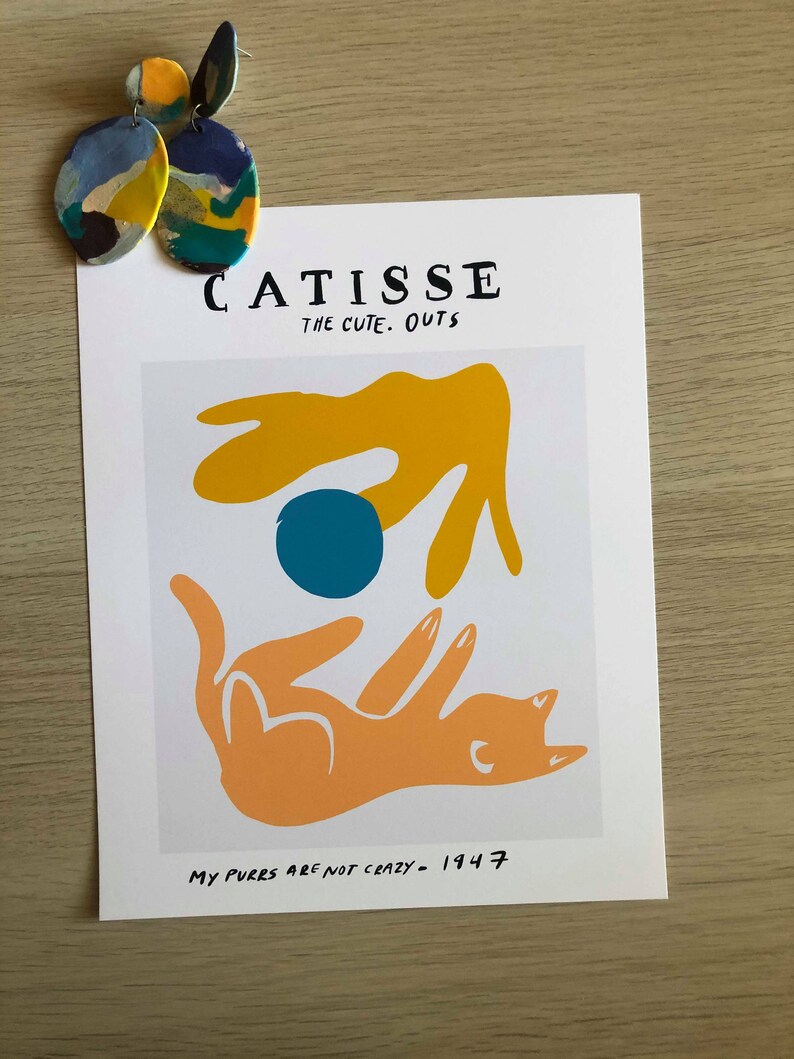 May include: A white print with a yellow, orange, and blue abstract design. The print has the text "CATISSE THE CUTE. OUTS" and "MY PURES ARE NOT CRAZY - 1947".