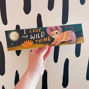 May include: A rectangular art print featuring a whimsical cat-mermaid illustration with the text "I LOVE MY WILD THING." The cat has orange and pink stripes, a pink fin, and a pink halo. The background is a night scene with a moon and stars.