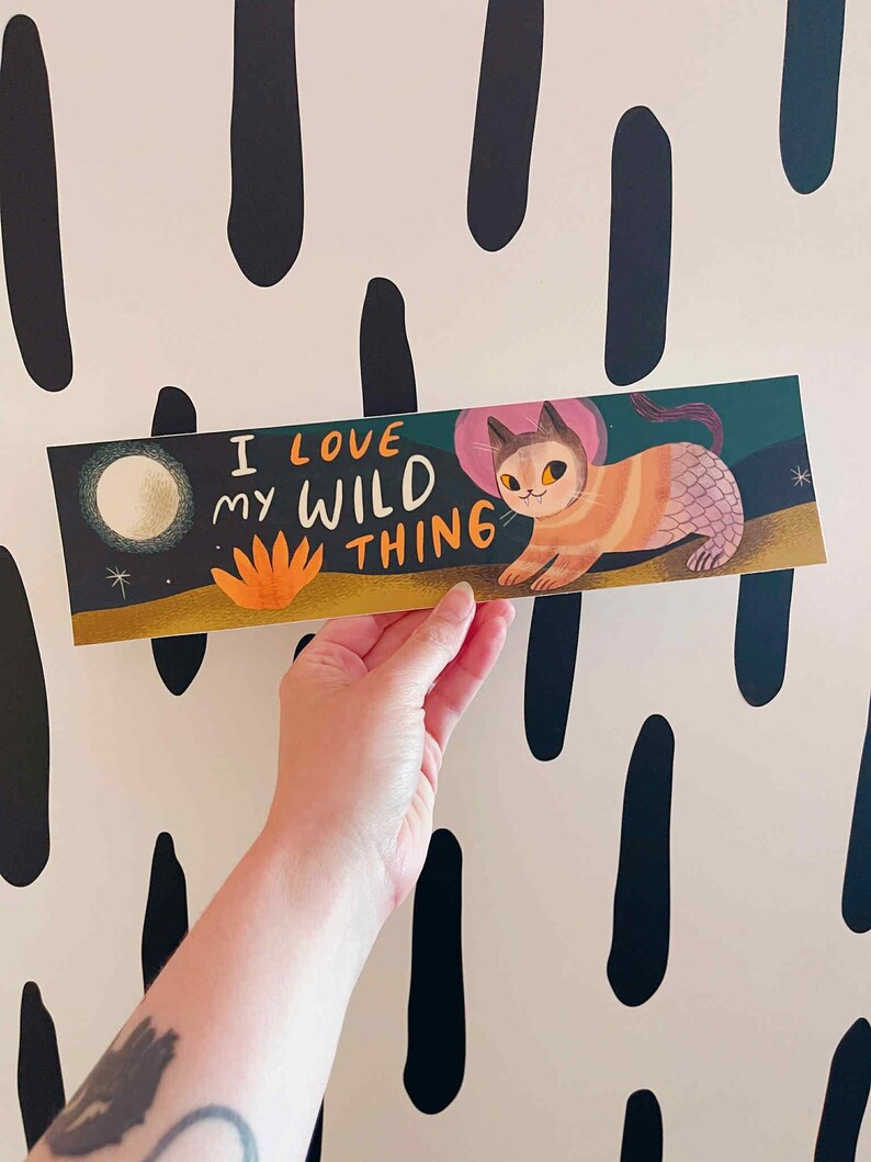 May include: A rectangular art print featuring a whimsical cat-mermaid illustration with the text "I LOVE MY WILD THING." The cat has orange and pink stripes, a pink fin, and a pink halo. The background is a night scene with a moon and stars.
